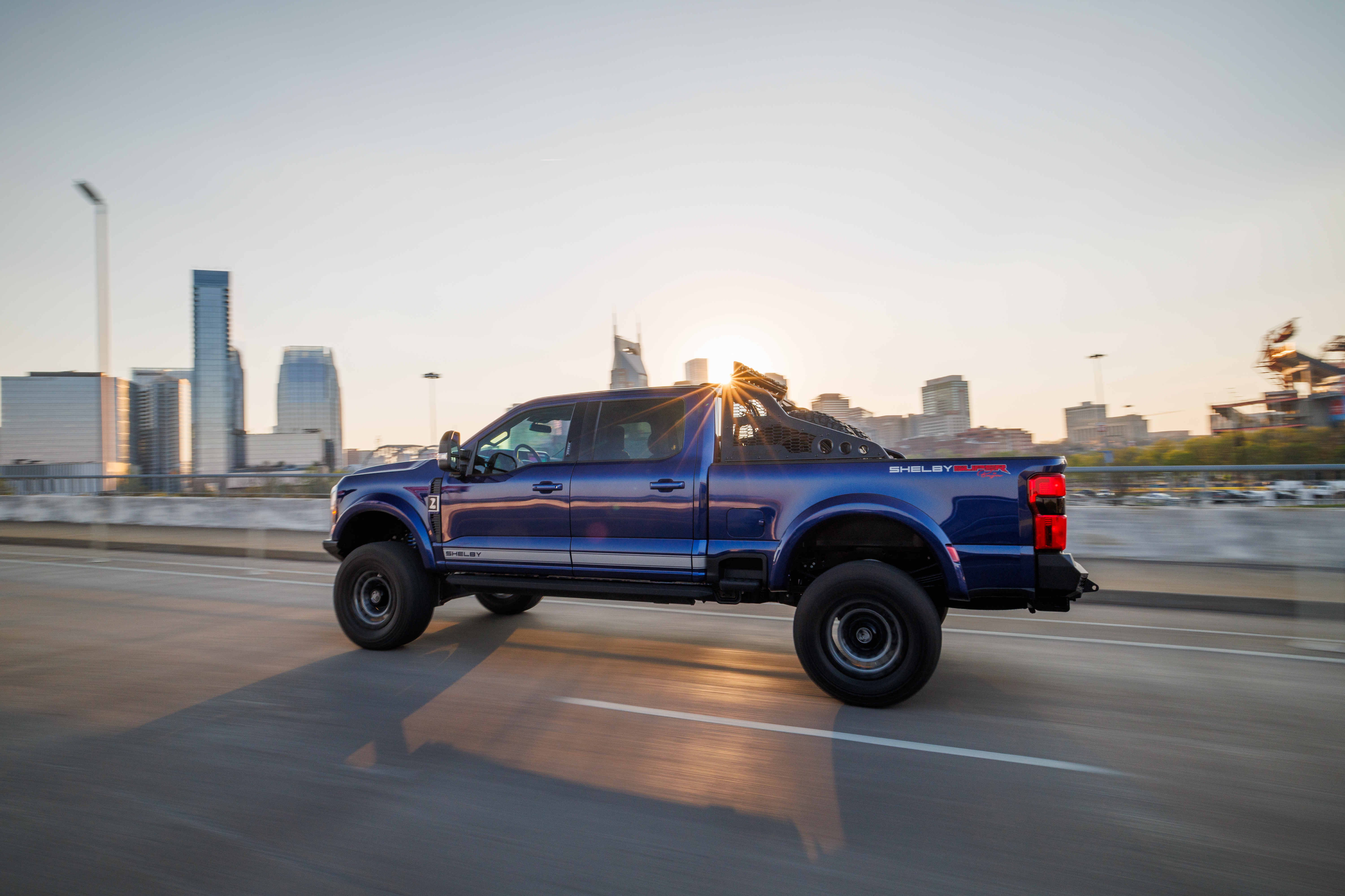 Shelby truck moving across a city bridge with skyline in the distance